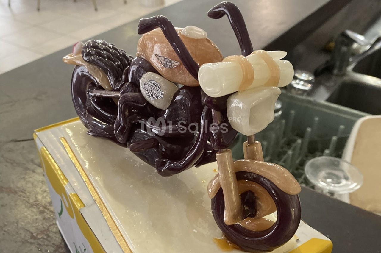 Sculpture miniature d'une moto réalisée en matériaux comestibles, posée sur une surface blanche.