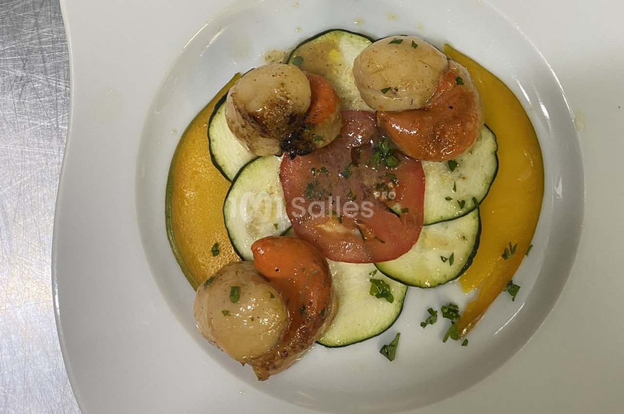 Assiette de noix de Saint-Jacques poêlées, disposées sur des tranches de courgettes, tomate et purée de légumes.
