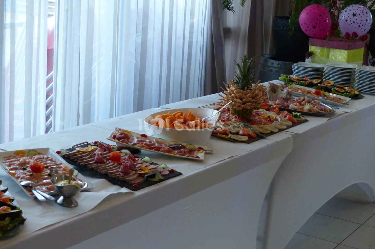 Buffet de plats variés disposés sur une table blanche, comprenant charcuterie, fruits et autres amuse-bouches.