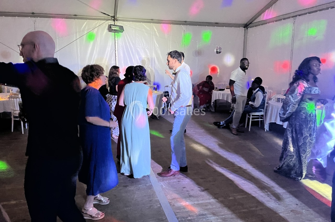 Personnes dansant sous des lumières colorées dans une salle sous chapiteau.