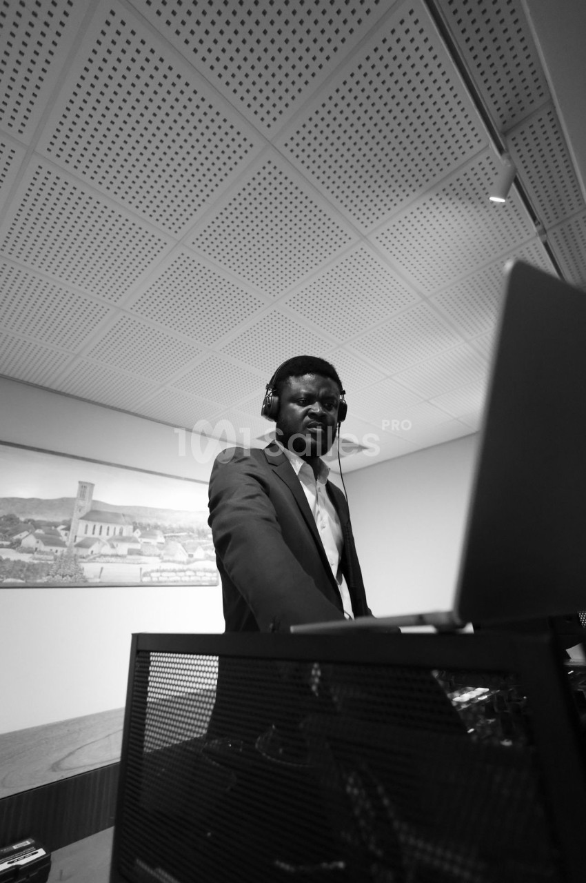 Un homme en costume utilise un ordinateur portable, portant un casque audio, dans une pièce au plafond perforé.