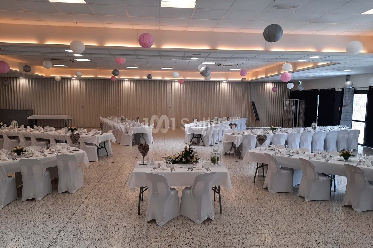 Salle de réception décorée avec des tables dressées, nappes blanches et suspensions colorées au plafond.