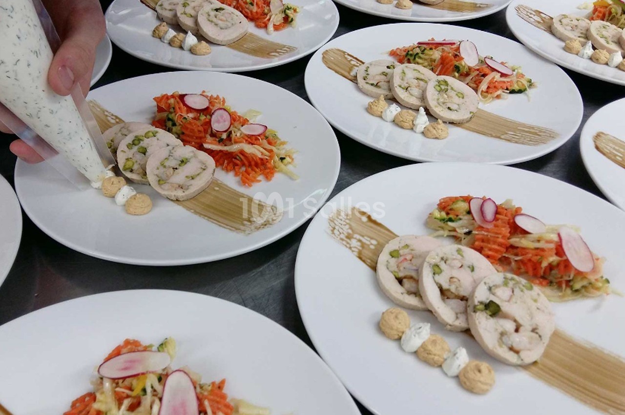 Assiettes dressées avec des roulés de volaille, légumes râpés et décorations de sauce, en préparation en cuisine.