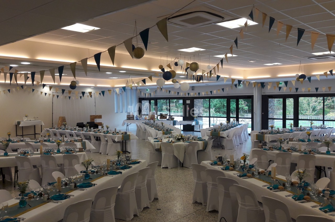 Salle de réception décorée avec des guirlandes et des tables dressées pour un événement festif.