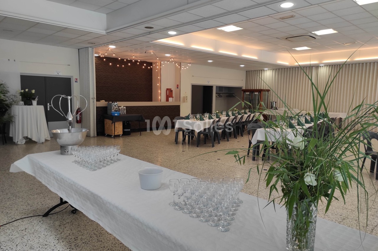 Salle de réception lumineuse avec tables dressées, plantes décoratives et espace pour boissons sur une table blanche.