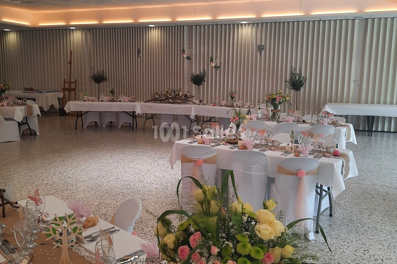 Salle de réception décorée pour un événement, avec tables dressées, fleurs et éclairage tamisé.