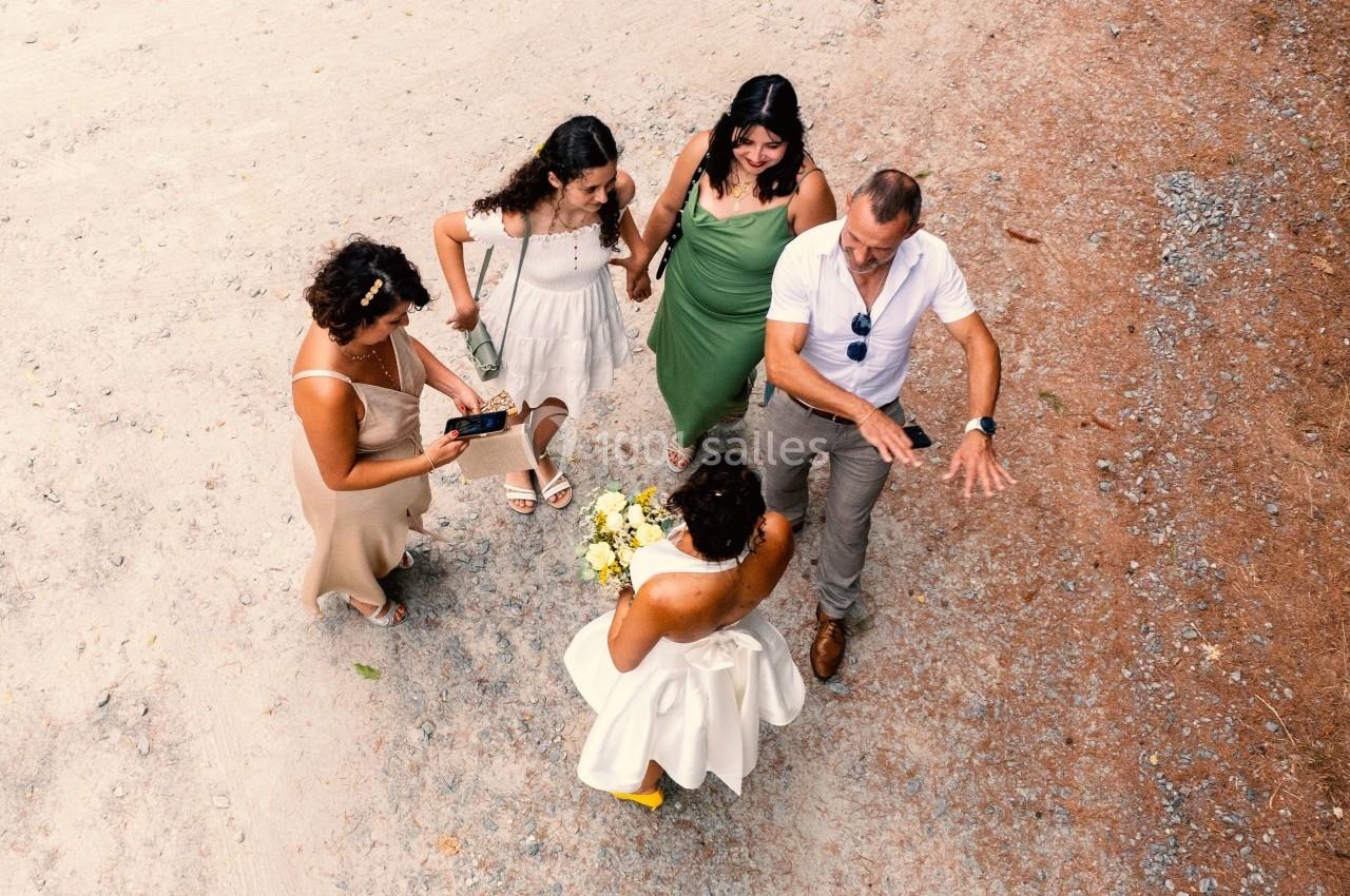 Vue aérienne de cinq personnes discutant sur un chemin en terre, dont une en robe blanche tenant un bouquet.
