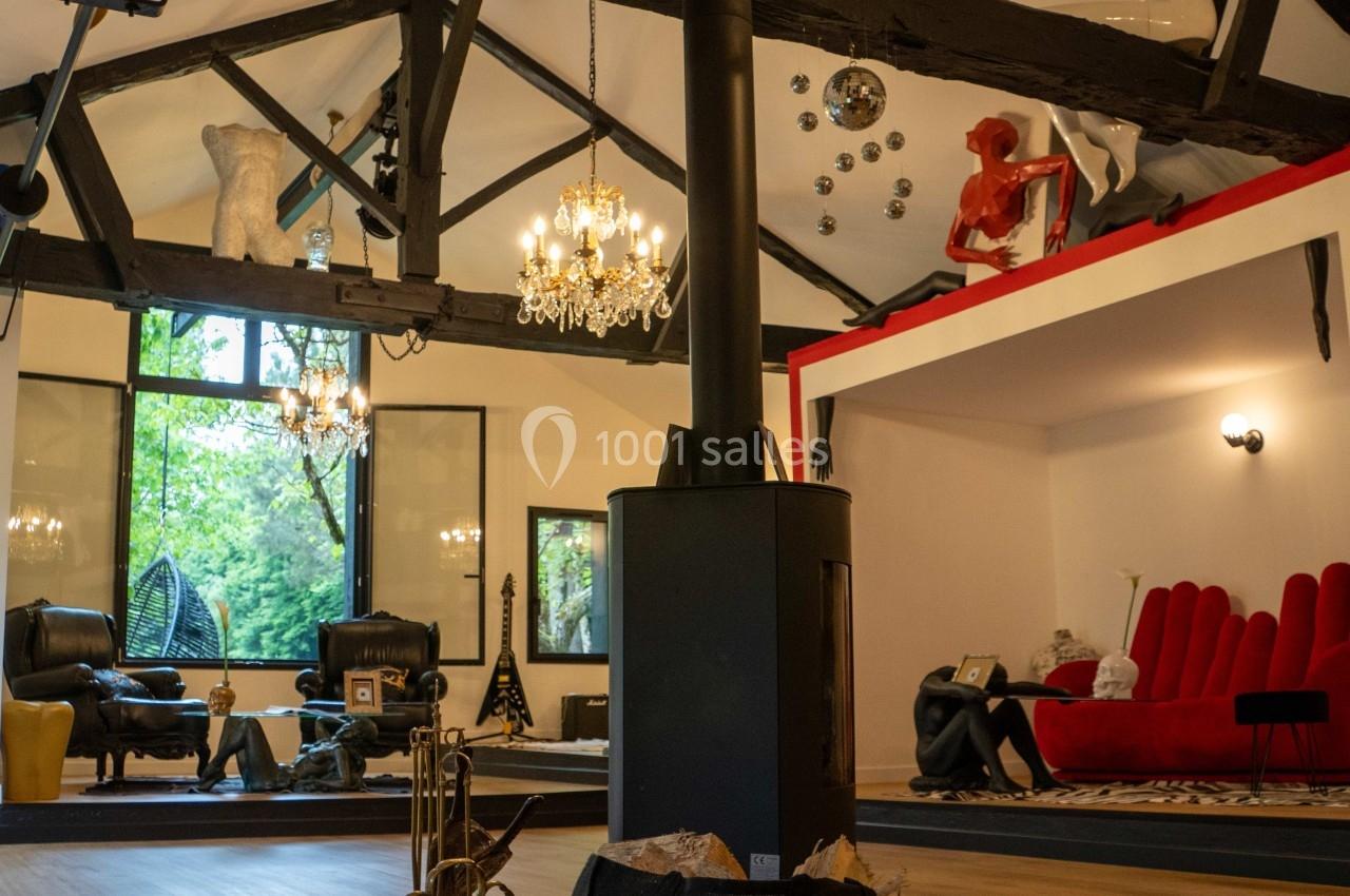 Intérieur d'un salon spacieux avec poutres apparentes, mobilier éclectique et grandes fenêtres donnant sur un jardin.