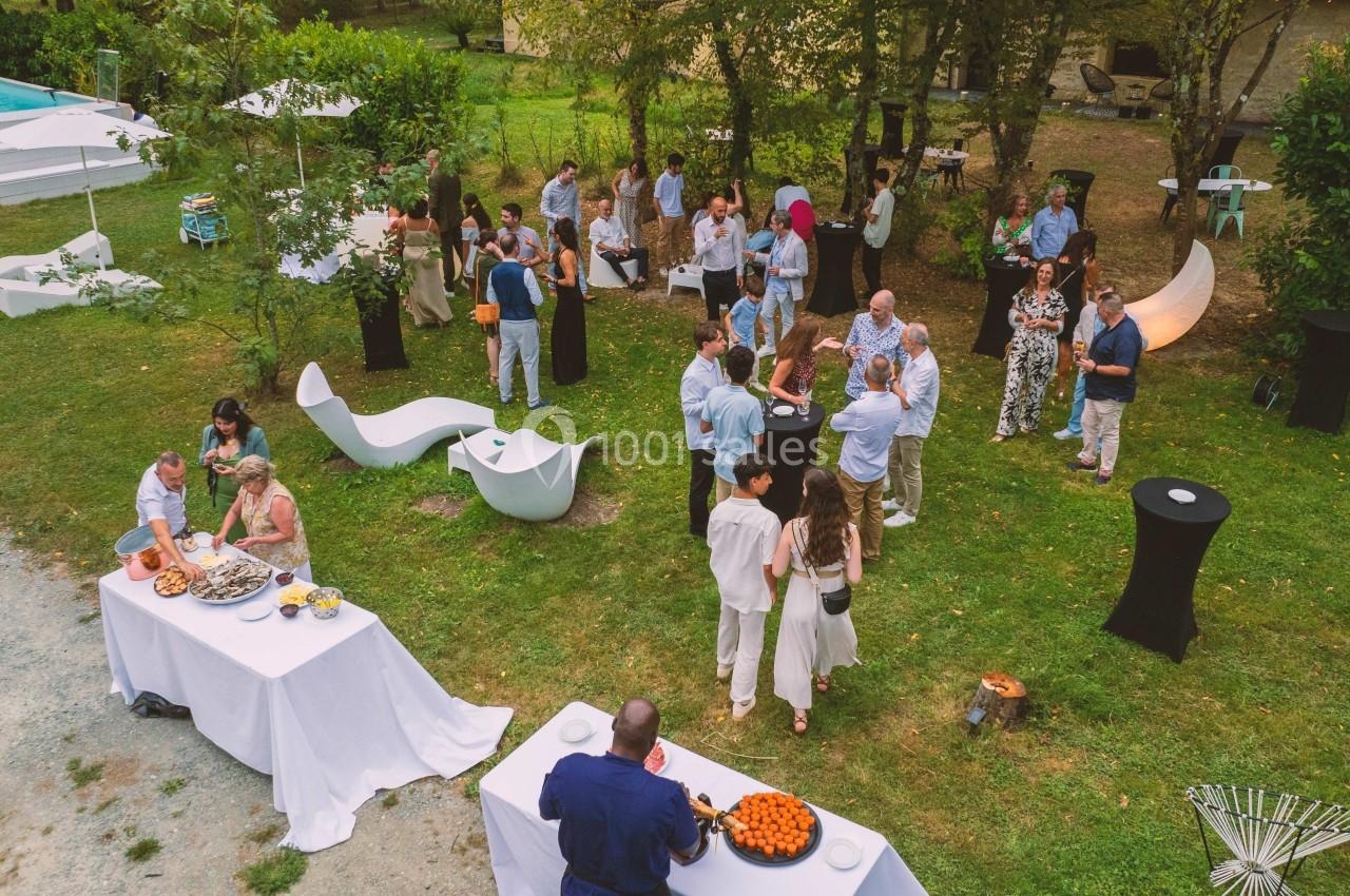 Groupe de personnes rassemblées dans un jardin pour un événement, avec tables de buffet et mobilier extérieur.