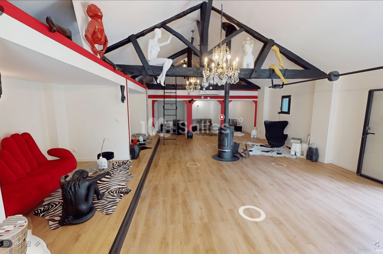 Salle spacieuse avec parquet, poutres apparentes, mobilier éclectique et sculptures colorées suspendues.