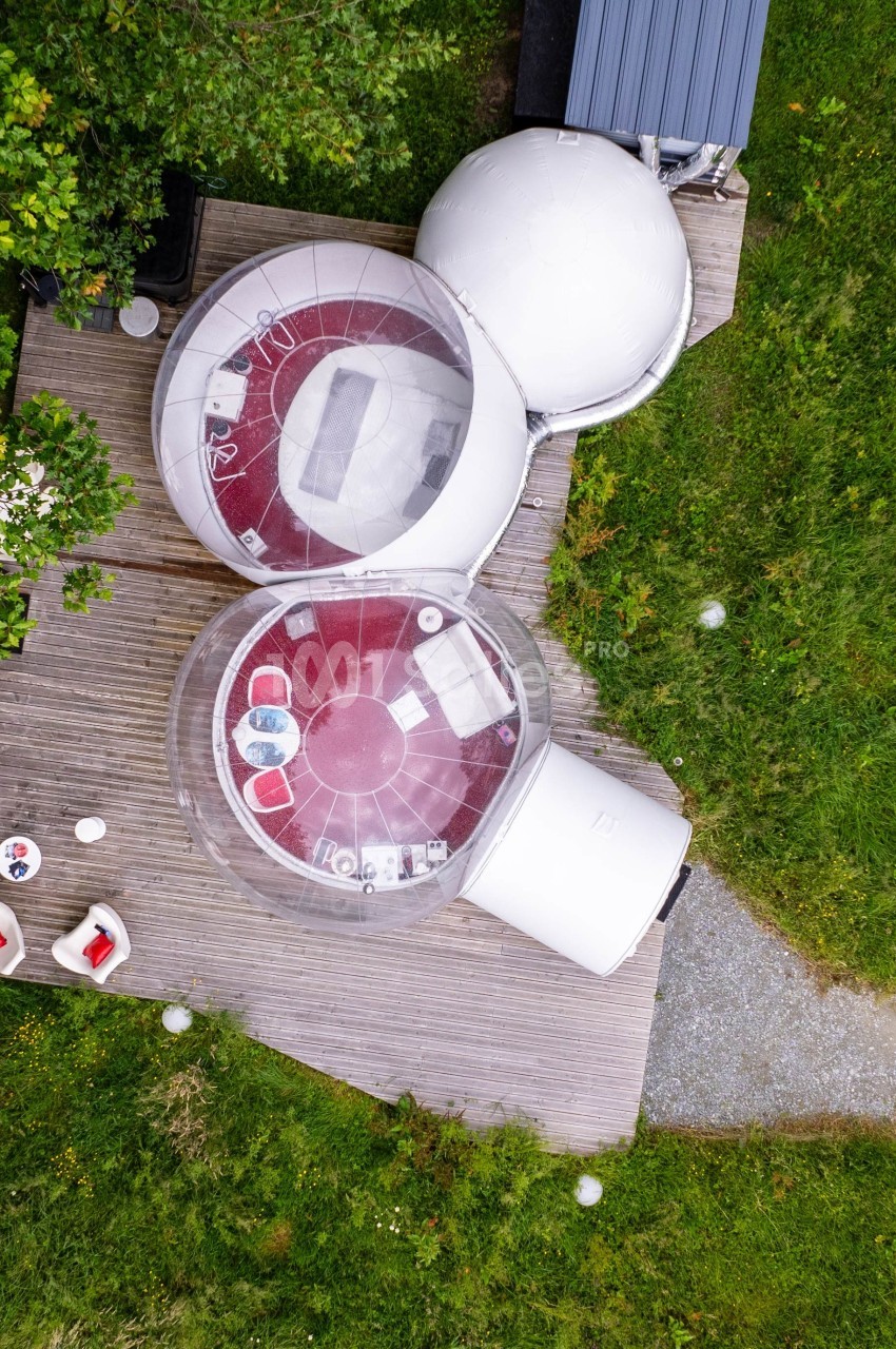 Vue aérienne de deux bulles transparentes aménagées sur une terrasse en bois, entourées de verdure.