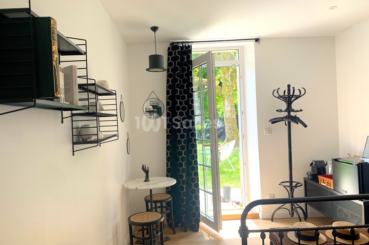 Chambre lumineuse avec porte-fenêtre ouverte sur un jardin, mobilier minimaliste et étagères murales.