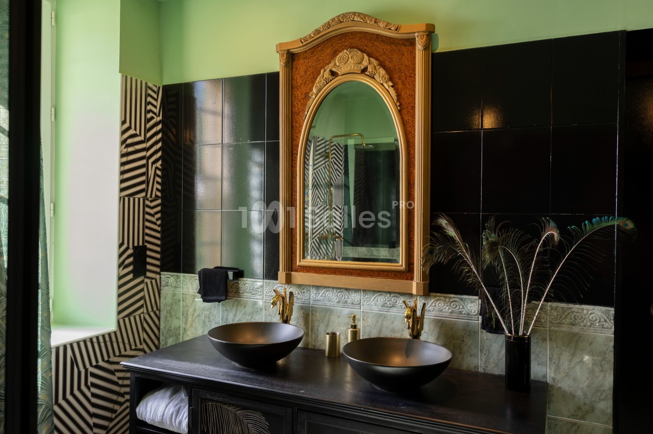 Salle de bain avec un grand miroir doré, deux vasques noires, robinetterie dorée et décoration moderne.