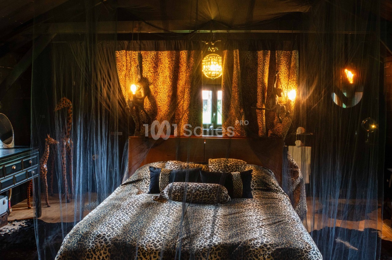 Chambre décorée dans un style safari avec lit à motifs léopard, moustiquaire et éclairage tamisé.