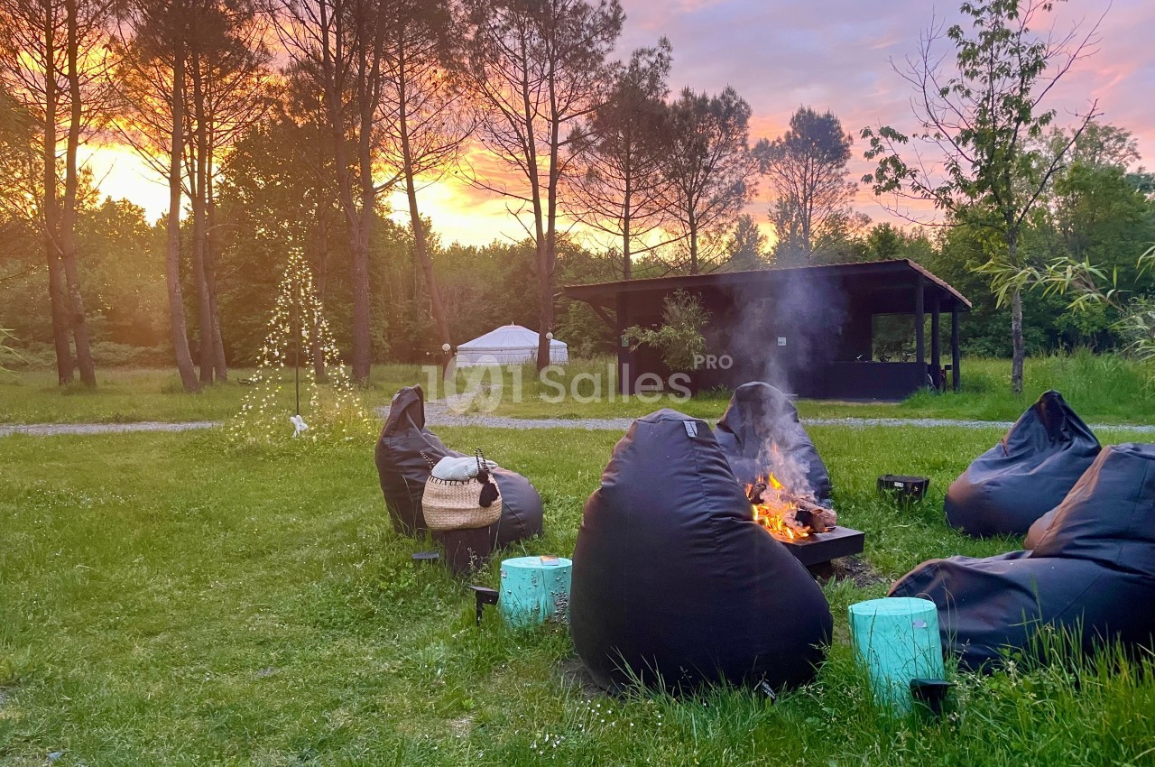 Des fauteuils en toile entourent un feu de camp dans un jardin verdoyant au coucher du soleil.