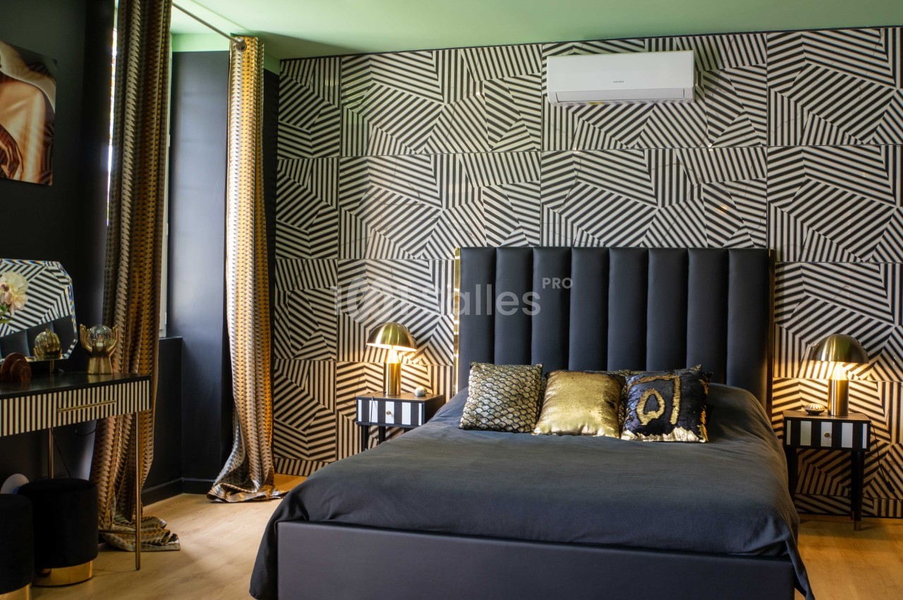 Chambre moderne avec lit noir, coussins dorés, murs à motifs géométriques et éclairage tamisé.