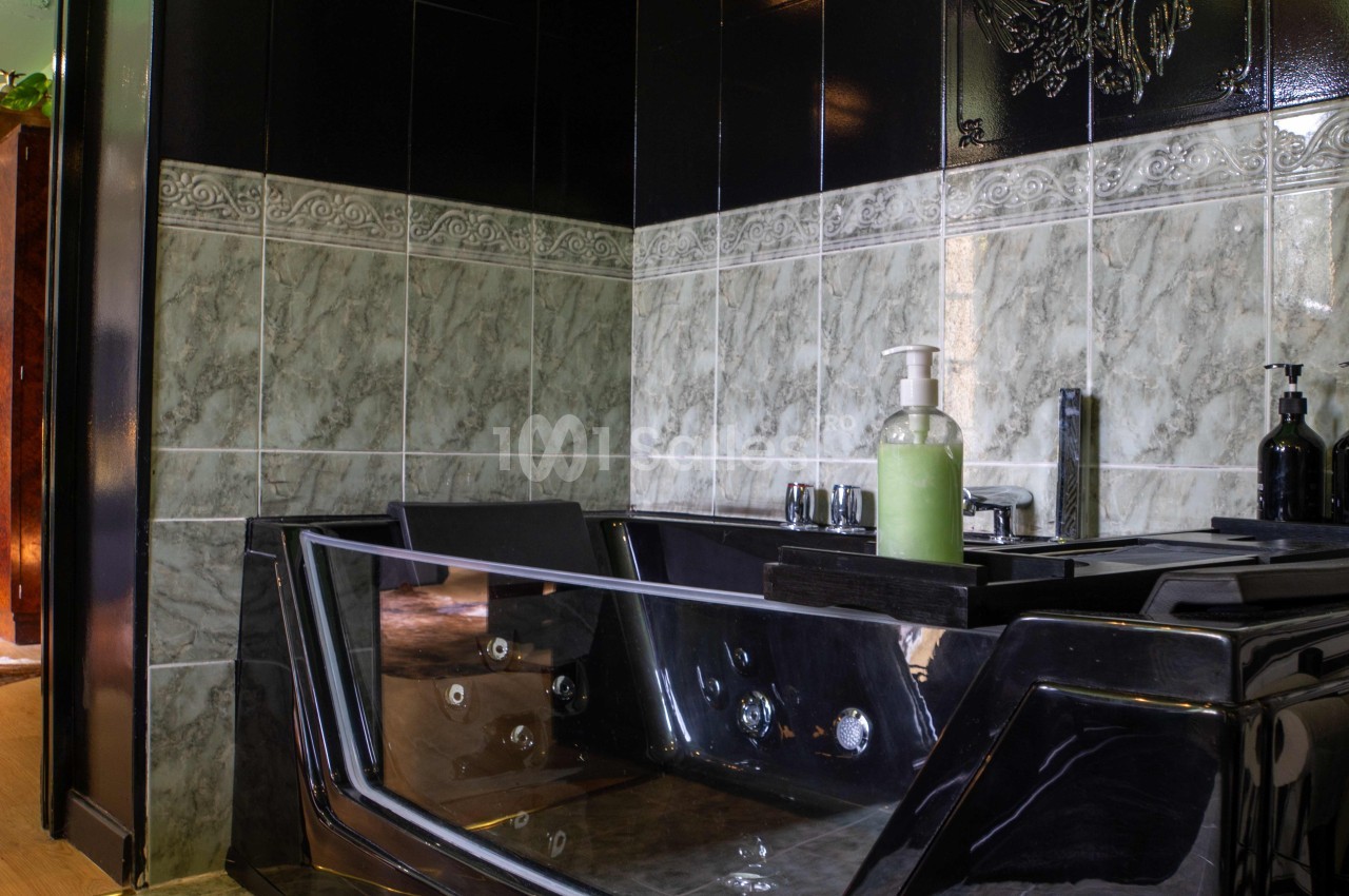 Baignoire noire moderne avec jets intégrés, entourée de carrelage gris et noir dans une salle de bain élégante.