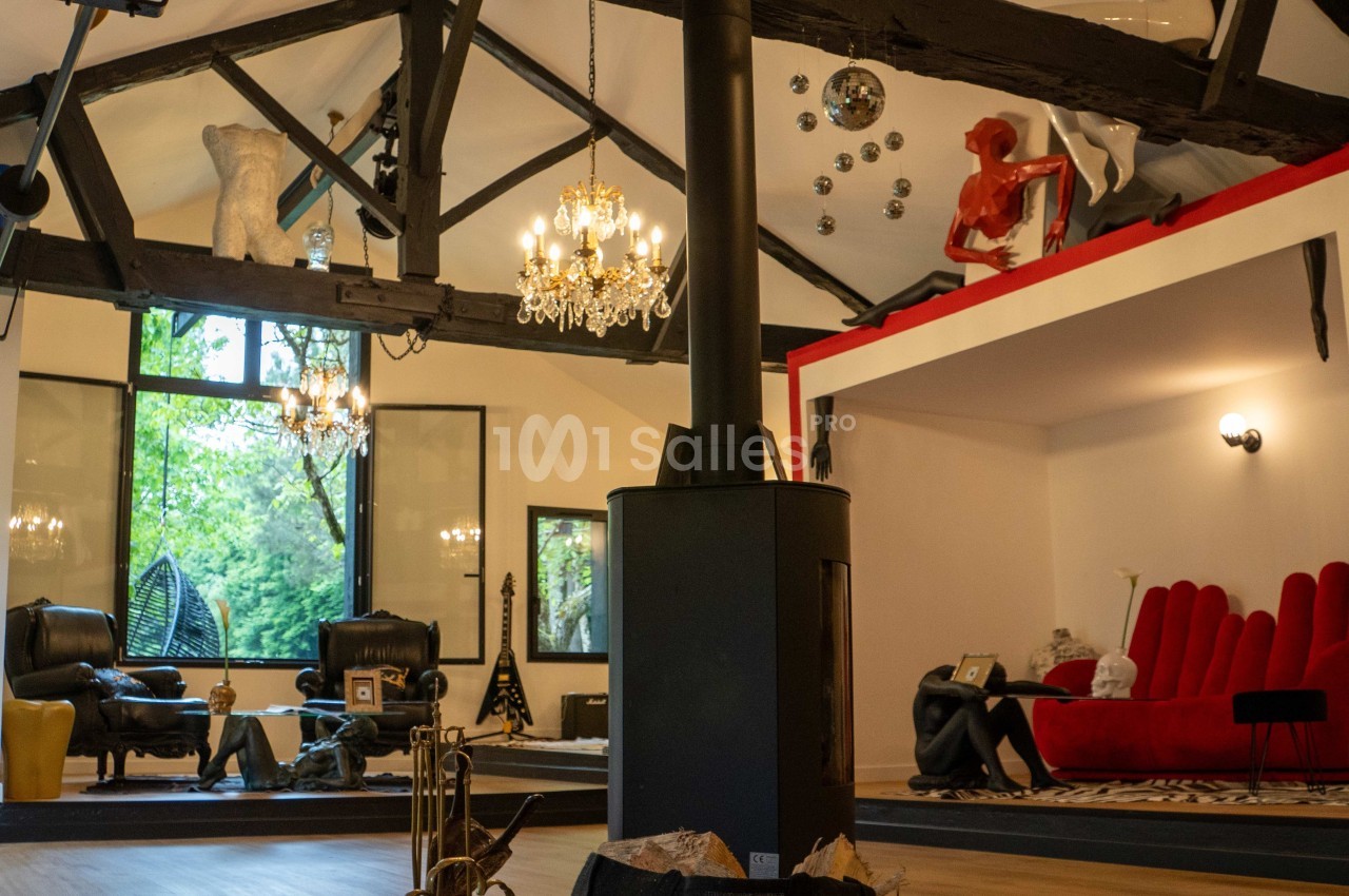 Intérieur d'un salon spacieux avec poutres apparentes, mobilier éclectique et grandes fenêtres donnant sur un jardin.