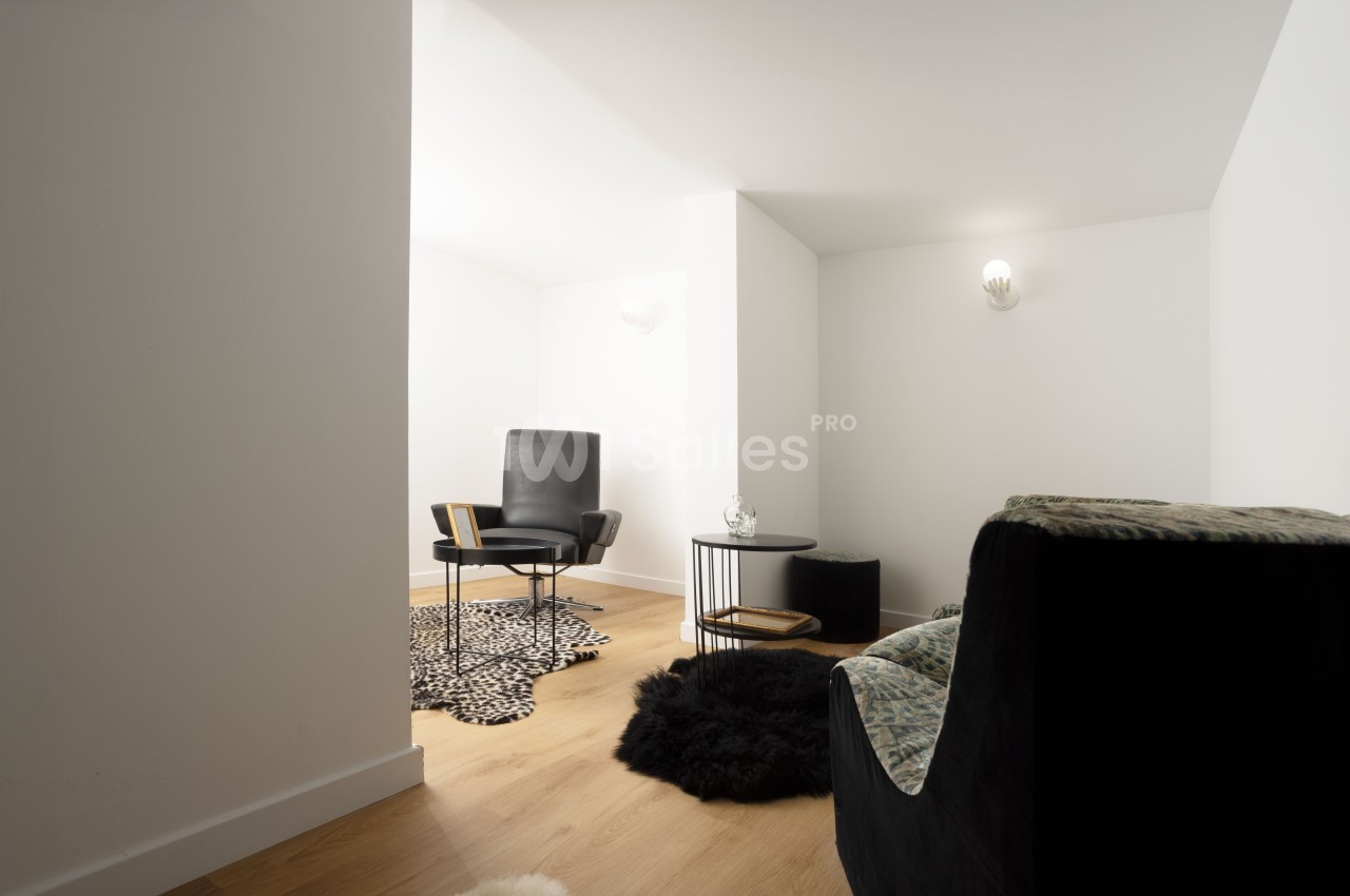 Espace intérieur minimaliste avec fauteuil noir, table basse ronde, tapis à motifs et sol en bois clair.