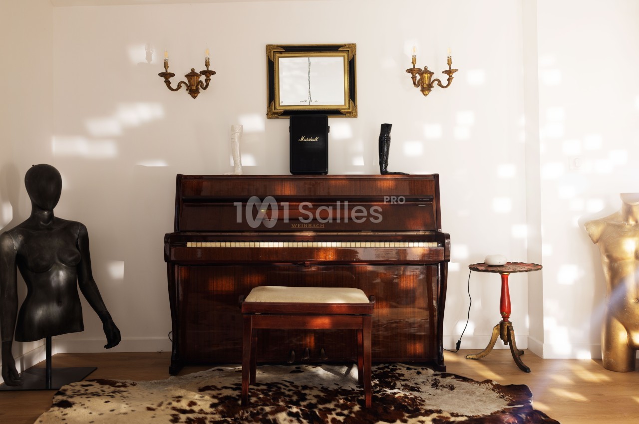 Un piano droit en bois dans une pièce décorée avec des sculptures, un tapis en peau et des appliques murales.