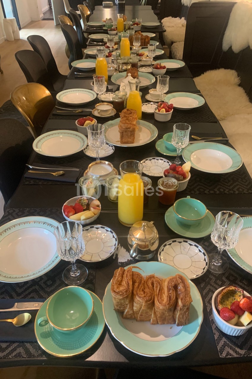 Table dressée pour un petit-déjeuner avec viennoiseries, fruits, jus d'orange et vaisselle élégante.