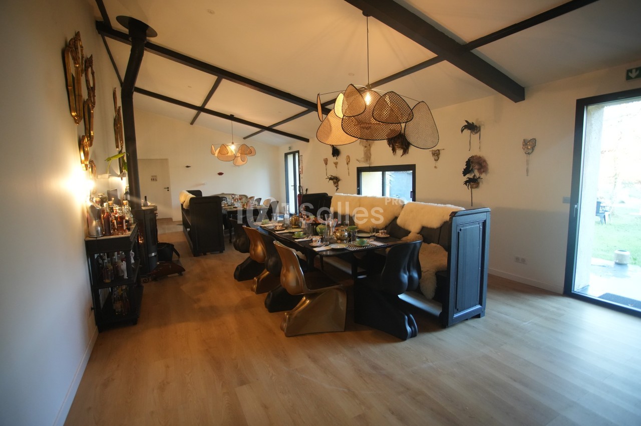 Salle à manger moderne avec table dressée, chaises design, luminaires suspendus et vue sur un jardin à travers une porte…