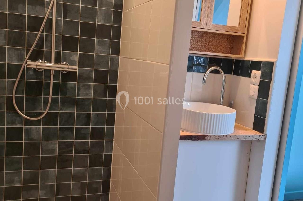 Douche avec carrelage sombre à gauche et meuble de salle de bain blanc avec vasque ronde à droite.