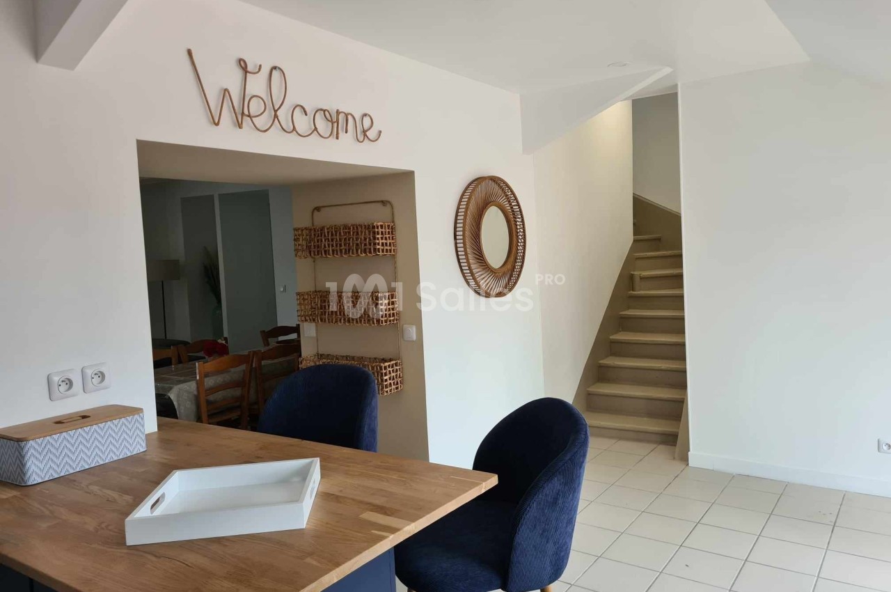 Cuisine ouverte avec comptoir en bois, chaises bleues, miroir rond, étagères murales et escalier en arrière-plan.