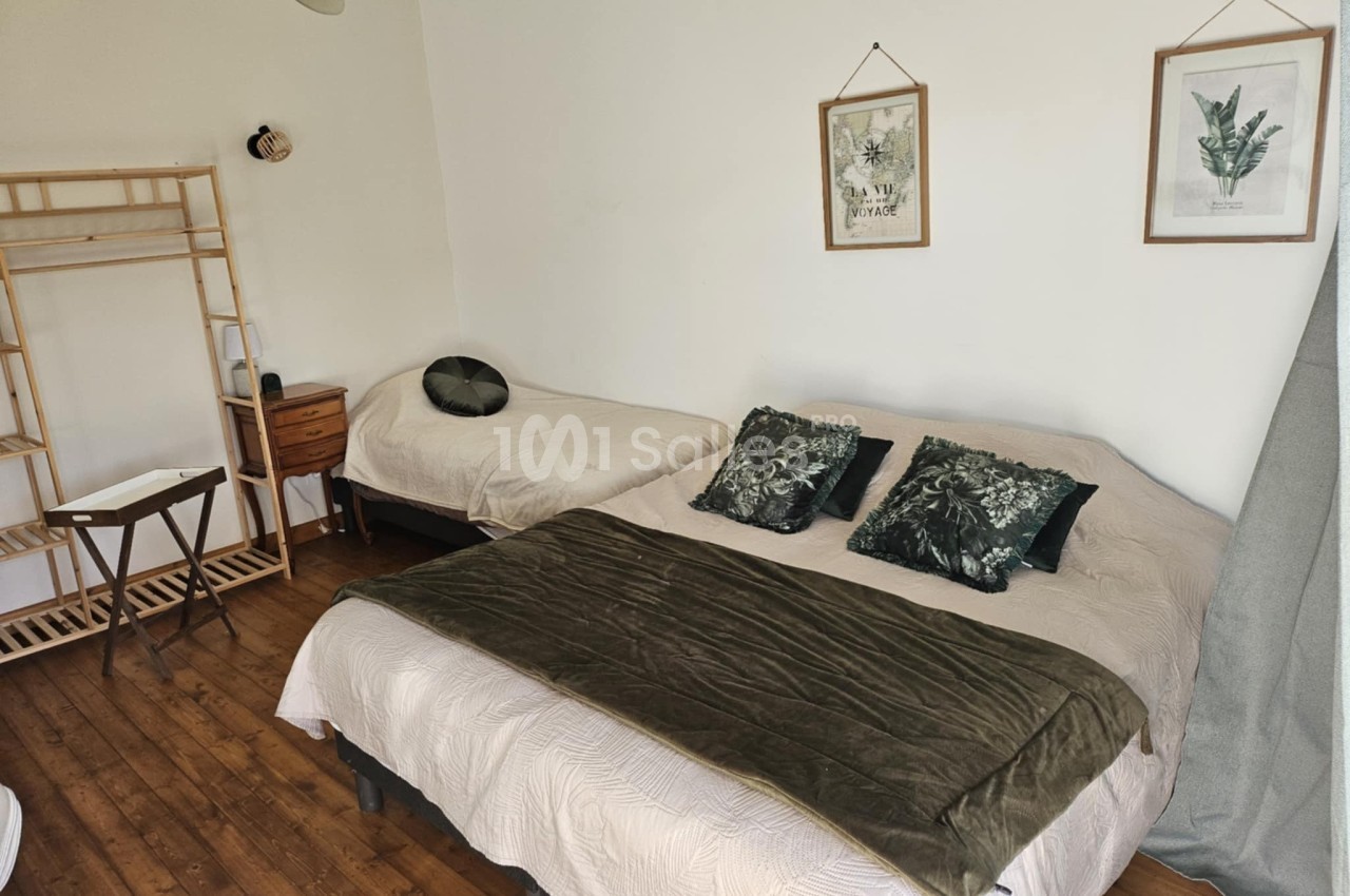 Chambre avec un lit double, un lit simple, des coussins verts, un portant en bois et des cadres décoratifs au mur.