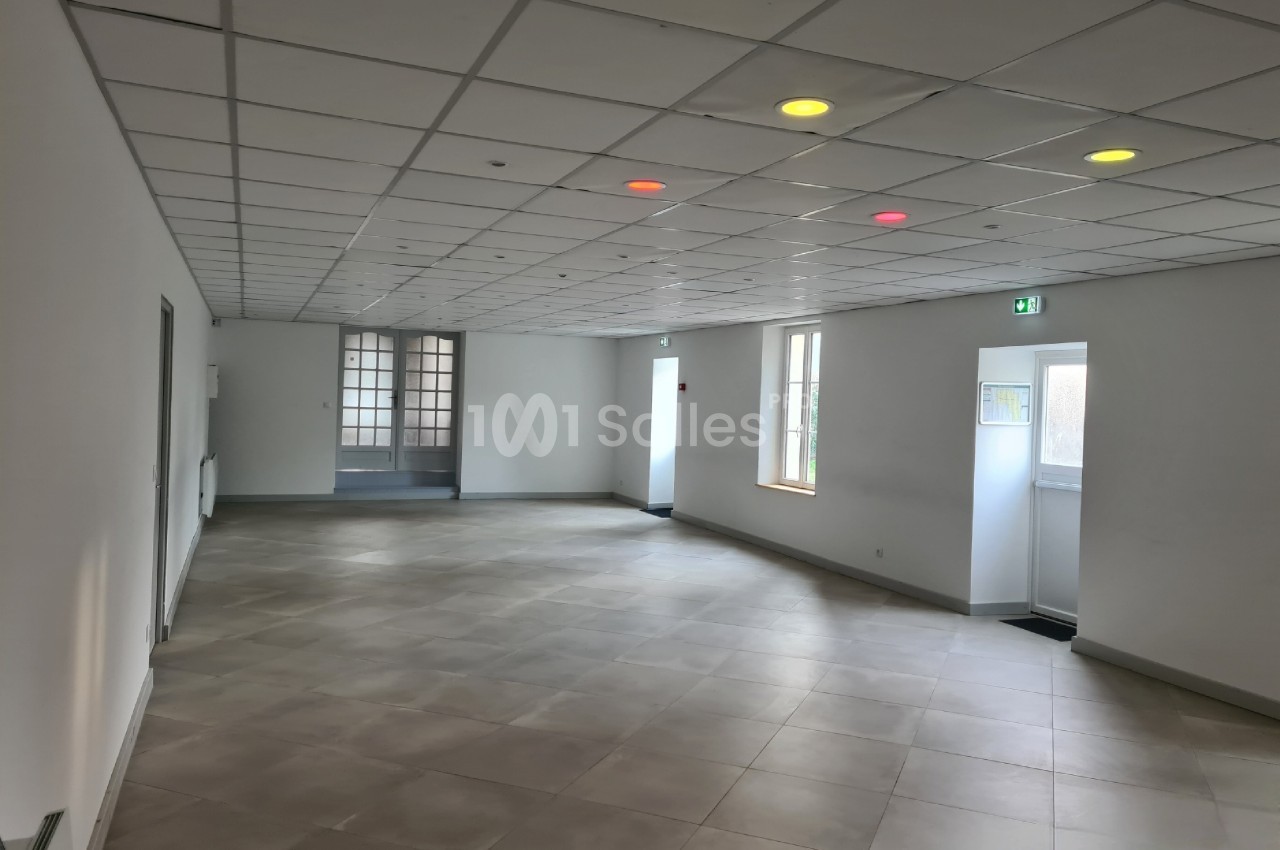 Salle vide avec carrelage clair, plafond à dalles blanches et quelques lumières colorées allumées.
