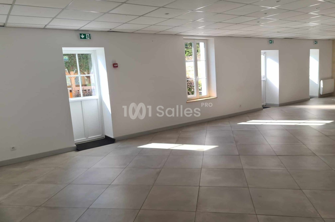 Salle lumineuse avec carrelage clair, murs blancs, fenêtres et portes donnant sur l'extérieur.