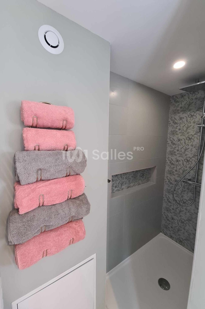 Salle de bain moderne avec douche à l'italienne, mur carrelé floral et serviettes pliées sur un porte-serviettes.