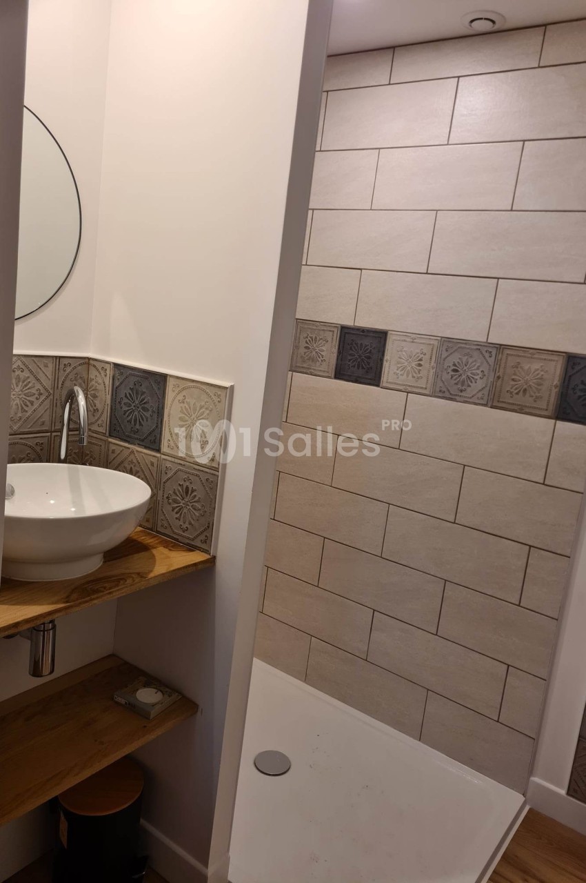 Salle de bain avec lavabo rond sur étagère en bois, miroir circulaire et douche avec carrelage beige et décoratif.