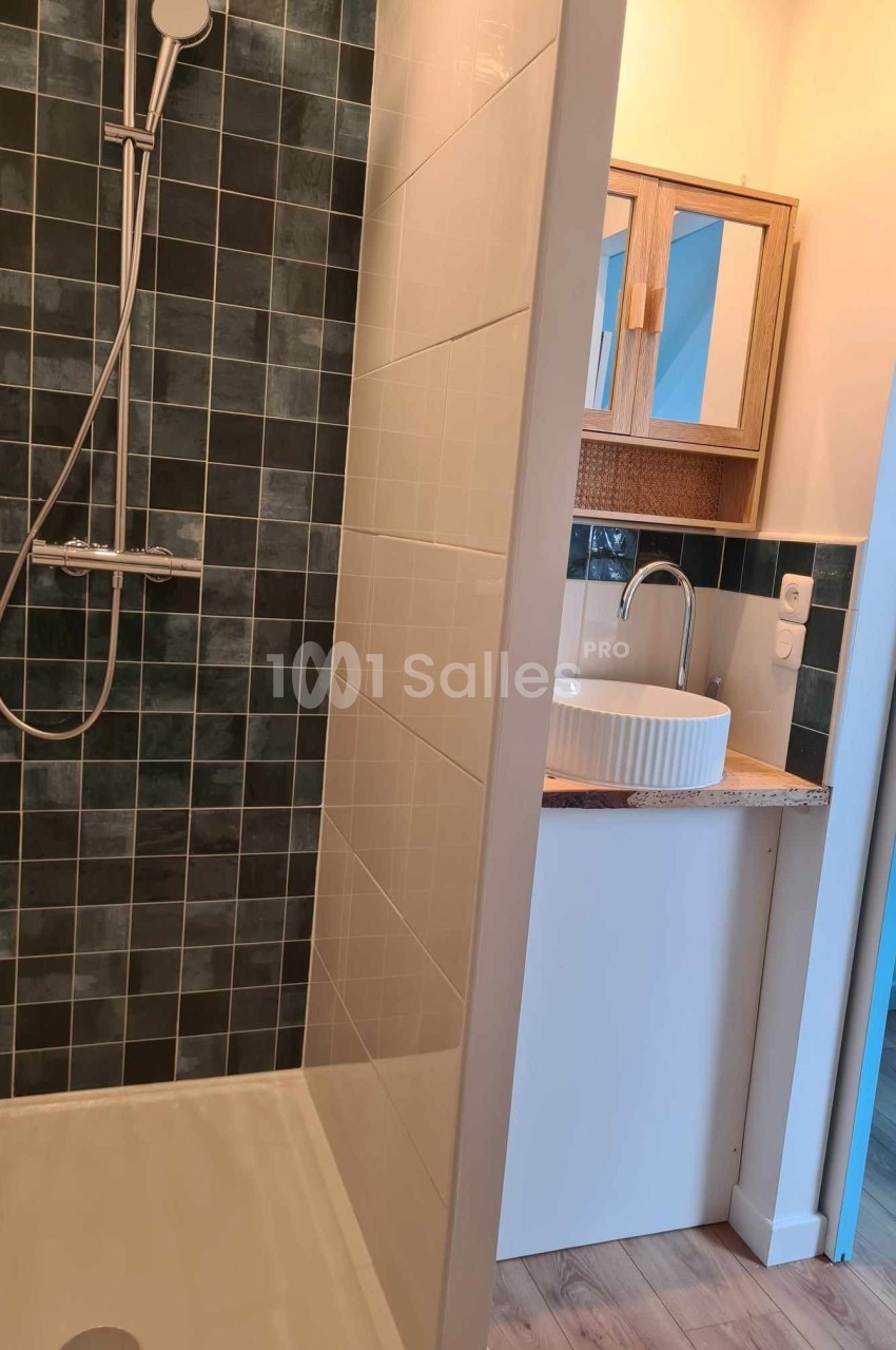Douche à l'italienne avec carrelage sombre à gauche et lavabo blanc sur meuble en bois à droite.