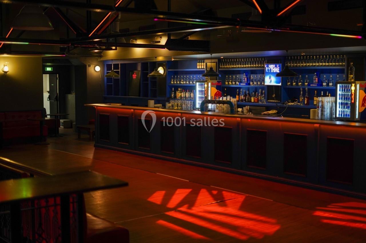 Intérieur d'un bar avec un long comptoir éclairé, des étagères de bouteilles et une ambiance tamisée.