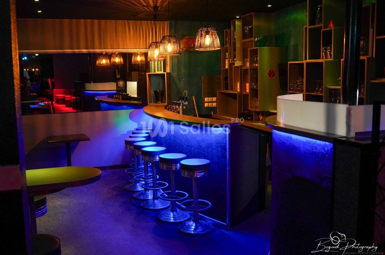 Un bar moderne avec des tabourets métalliques, éclairé par des lumières colorées dans une ambiance tamisée.