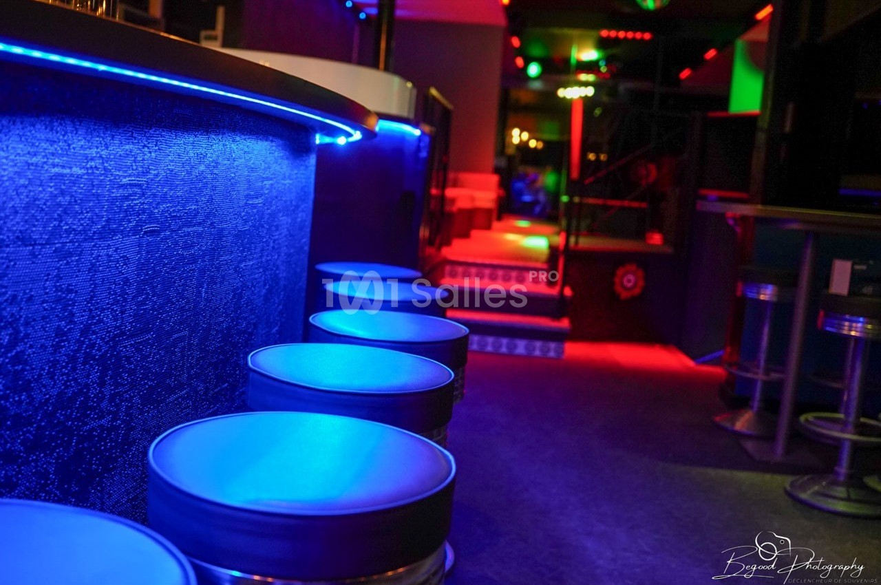 Tabourets alignés le long d'un bar éclairé par des lumières colorées dans un espace intérieur moderne et sombre.