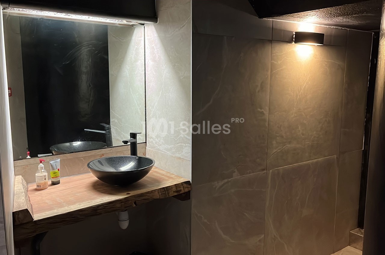 Vue d'une salle de bain avec un lavabo en vasque noire sur un plan en bois et un éclairage mural tamisé.
