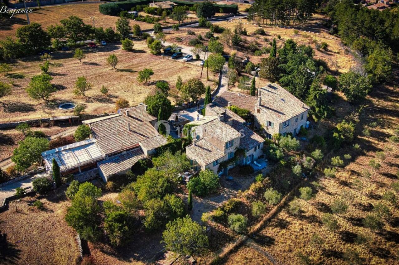 Vue aérienne d'une grande propriété en pierre entourée de végétation, située dans une campagne aride.