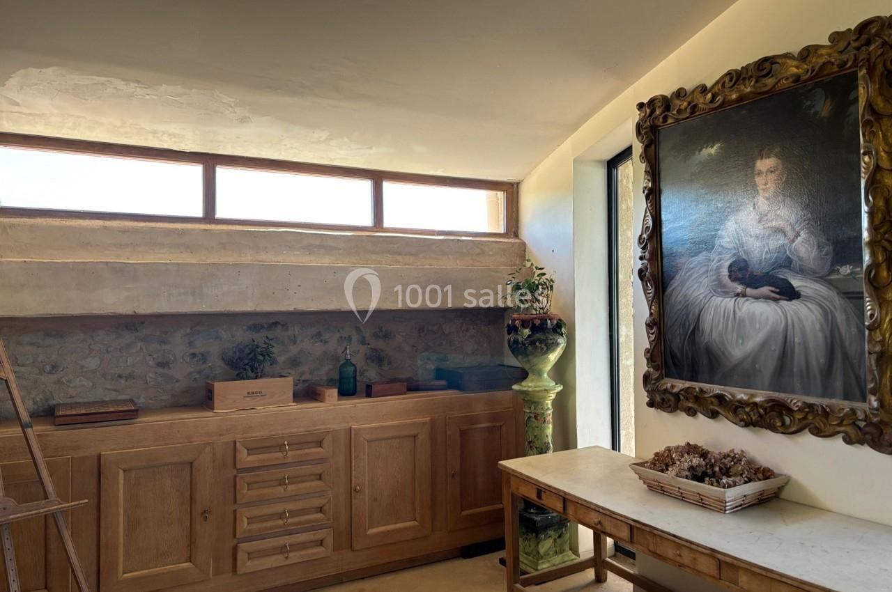 Intérieur lumineux avec un meuble en bois, une table, un tableau encadré et des éléments décoratifs.