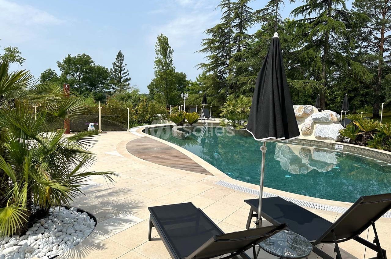 Piscine extérieure entourée de végétation, avec transats, parasols noirs et ciel dégagé en arrière-plan.