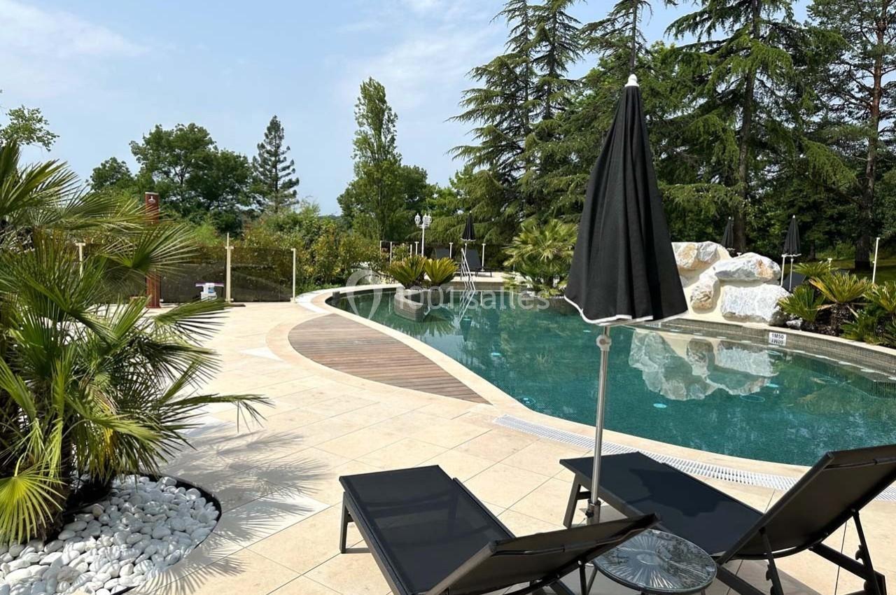 Piscine extérieure entourée de végétation, avec transats, parasols noirs et ciel dégagé en arrière-plan.