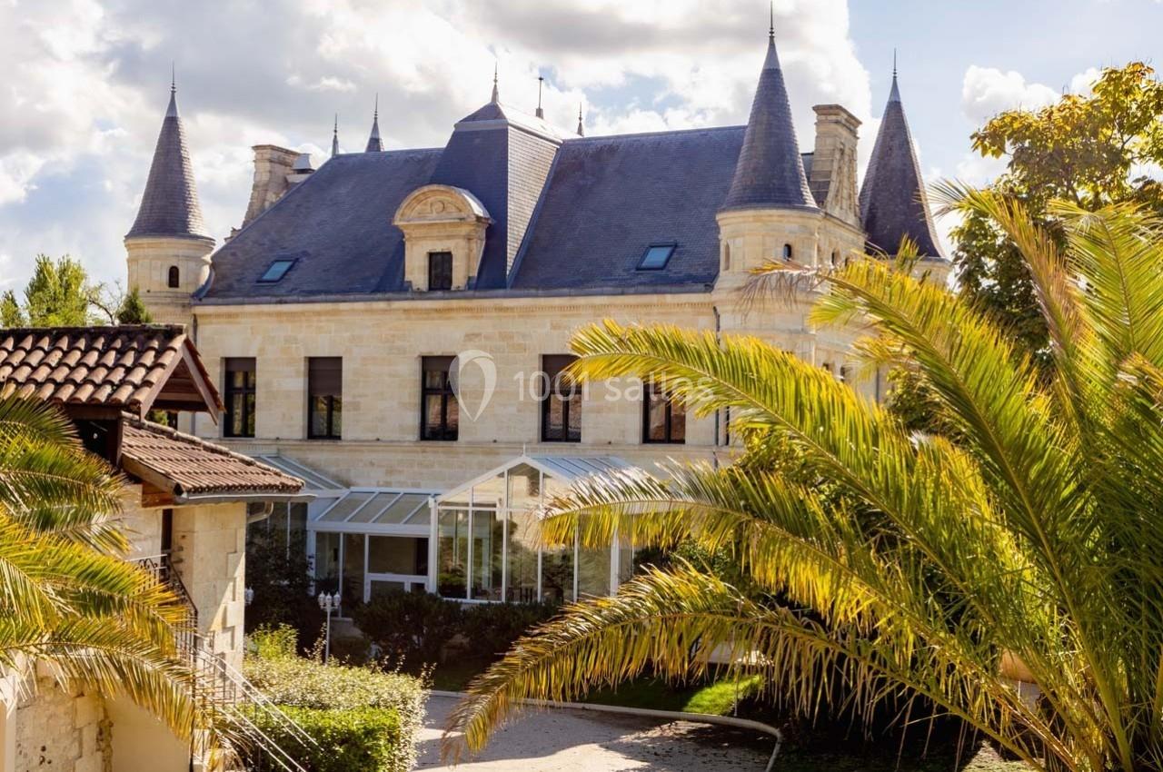 Façade d'un château en pierre avec des tourelles, entouré de végétation et éclairé par une lumière naturelle.