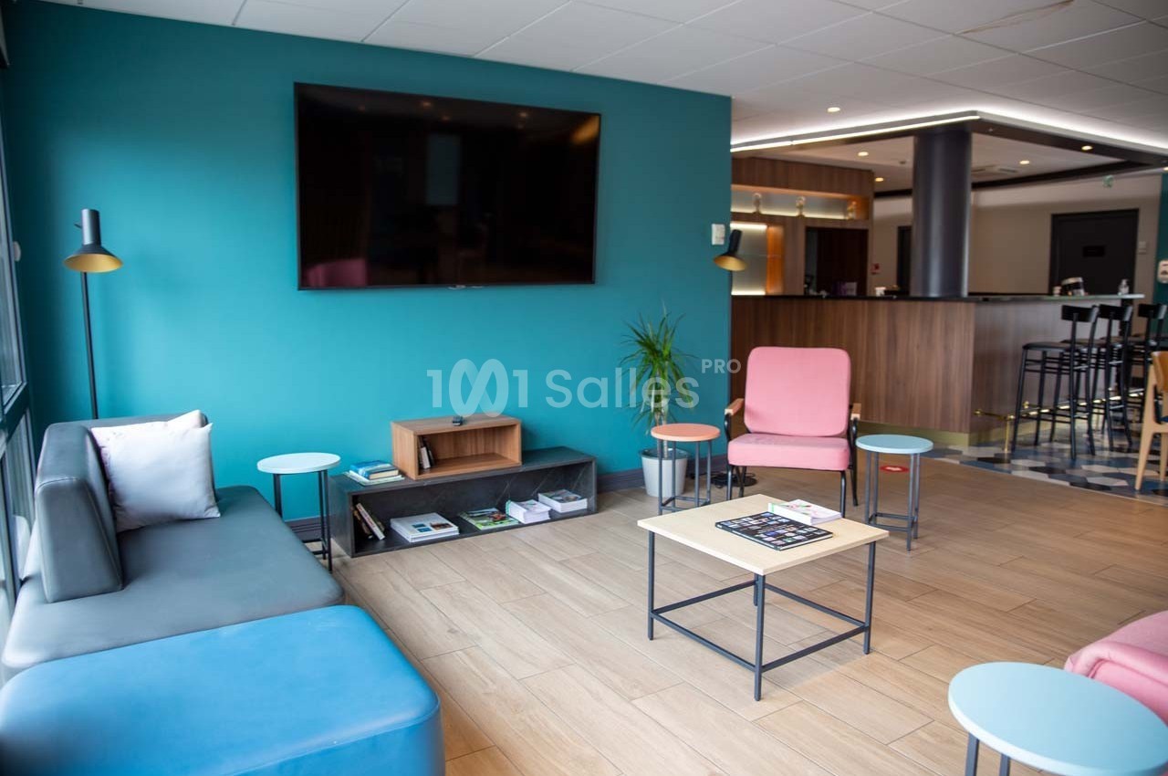 Salon moderne avec canapé, fauteuils colorés, table basse et télévision murale dans un espace lumineux.