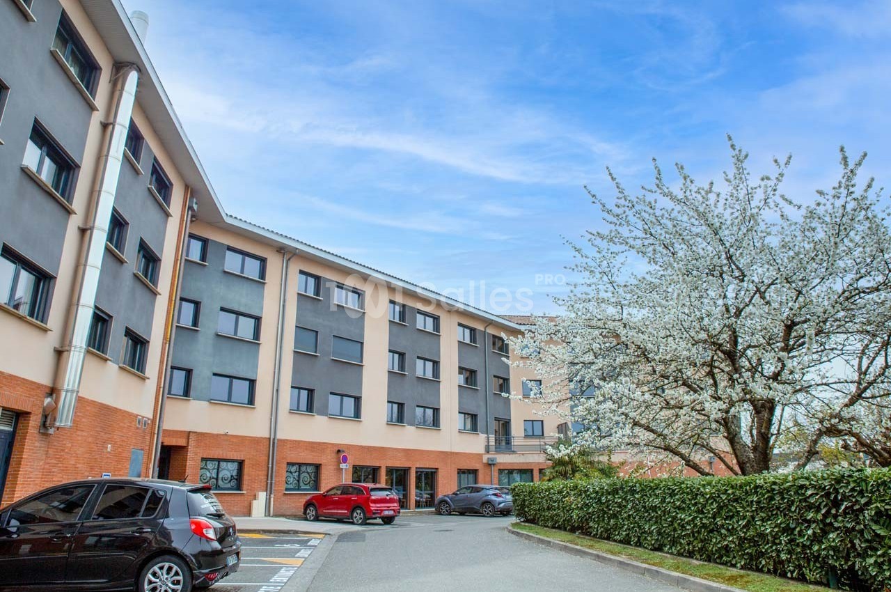 Façade d'un immeuble moderne avec des voitures stationnées et un arbre en fleurs au premier plan.