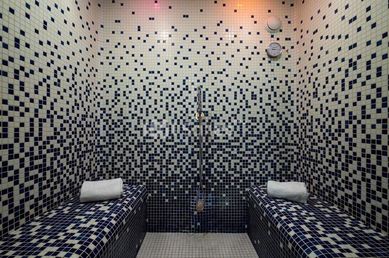 Salle de hammam avec murs et bancs en mosaïque bleue, équipée d'une douche murale et de serviettes pliées.