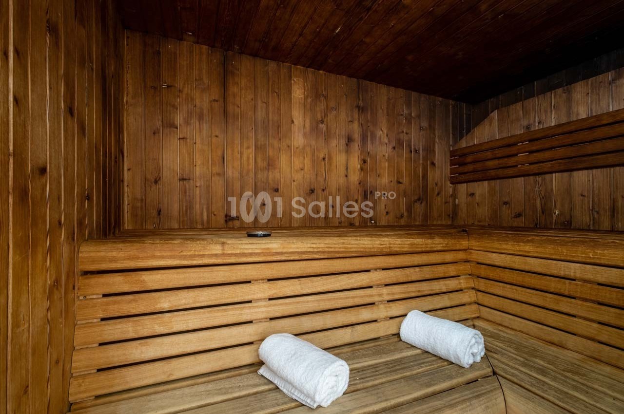 Intérieur d'un sauna en bois avec deux serviettes blanches roulées posées sur un banc.