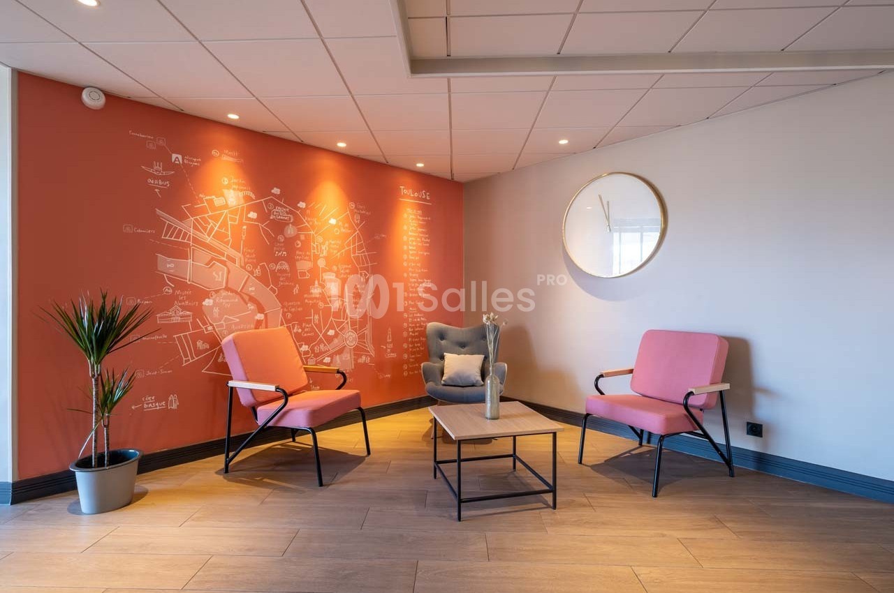 Espace d'attente avec deux fauteuils roses, une table basse, un fauteuil gris et un mur décoré d'une carte illustrée.