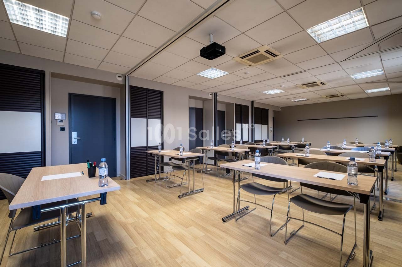 Salle de réunion moderne avec tables en bois, chaises alignées, bouteilles d'eau et matériel de prise de notes.