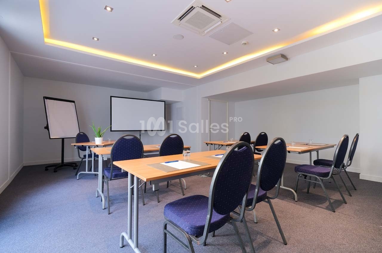 Salle de réunion lumineuse avec tables, chaises, tableau blanc et écran de projection.